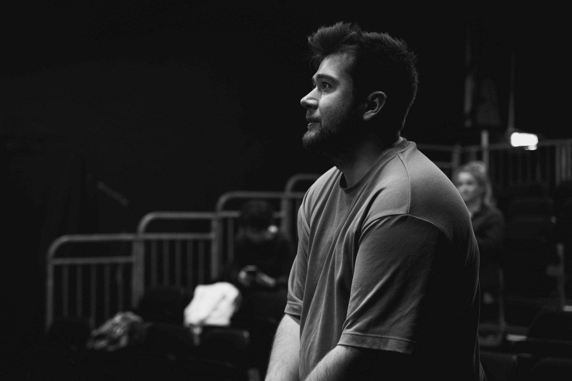 Dan Light in profile, watching the stage from a darkened auditorium during a technical rehearsal.